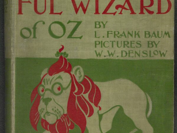 The green and red cover of the first edition of The Wonderful Wizard of Oz, with Denslow’s drawing of the Cowardly Lion wearing spectacles