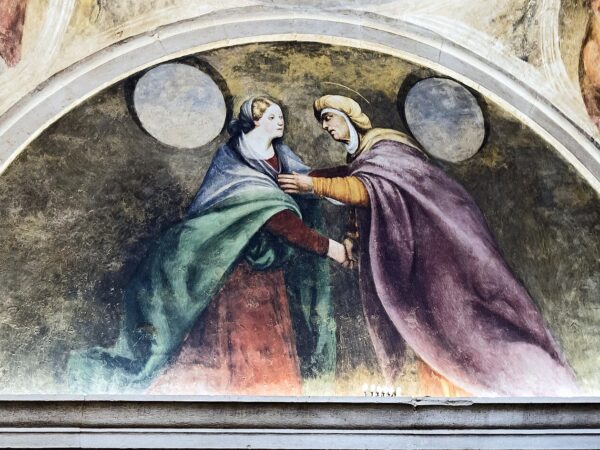 Mary greets her cousin Elizabeth, both expecting children, before a crowd of onlookers.