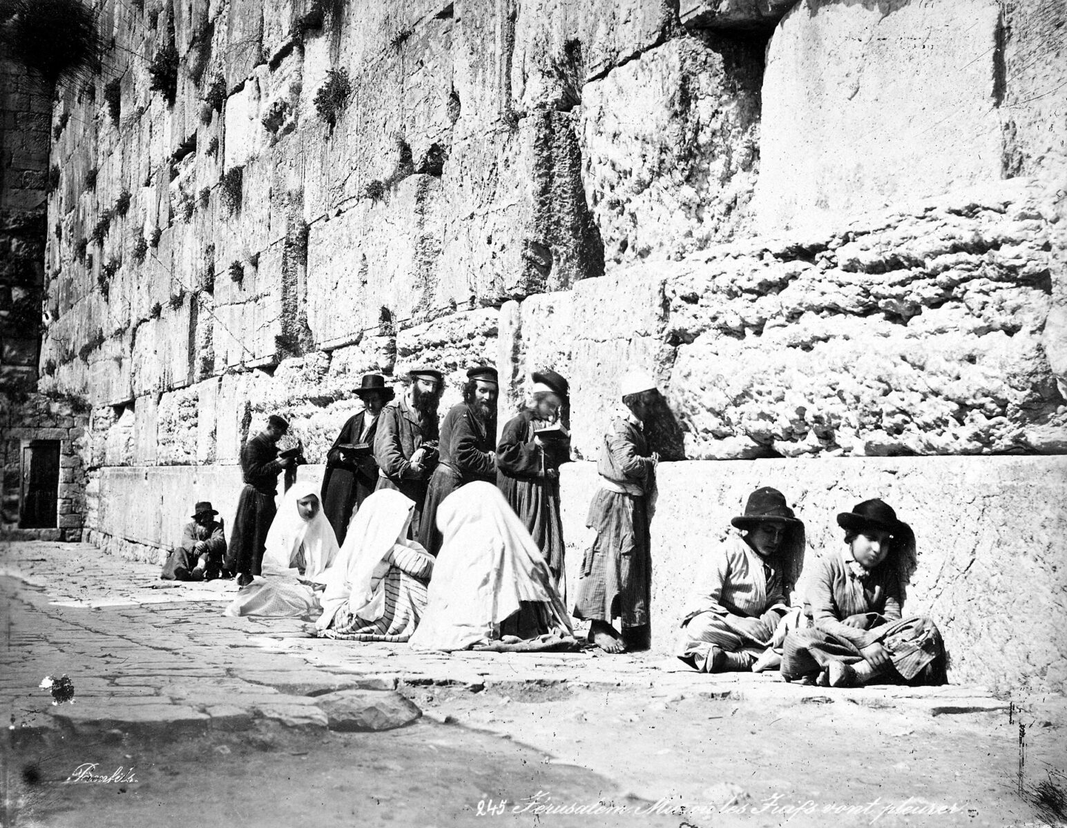 Jewish men in long coats pray beside the great stones of the Western Wall in Jerusalem.