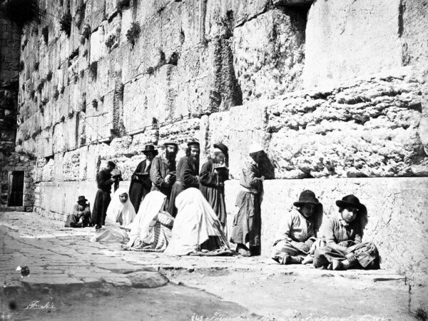 Jewish men in long coats pray beside the great stones of the Western Wall in Jerusalem.