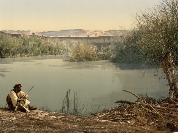 The River Jordan winding between trees and banks in a colour print from about 1900.