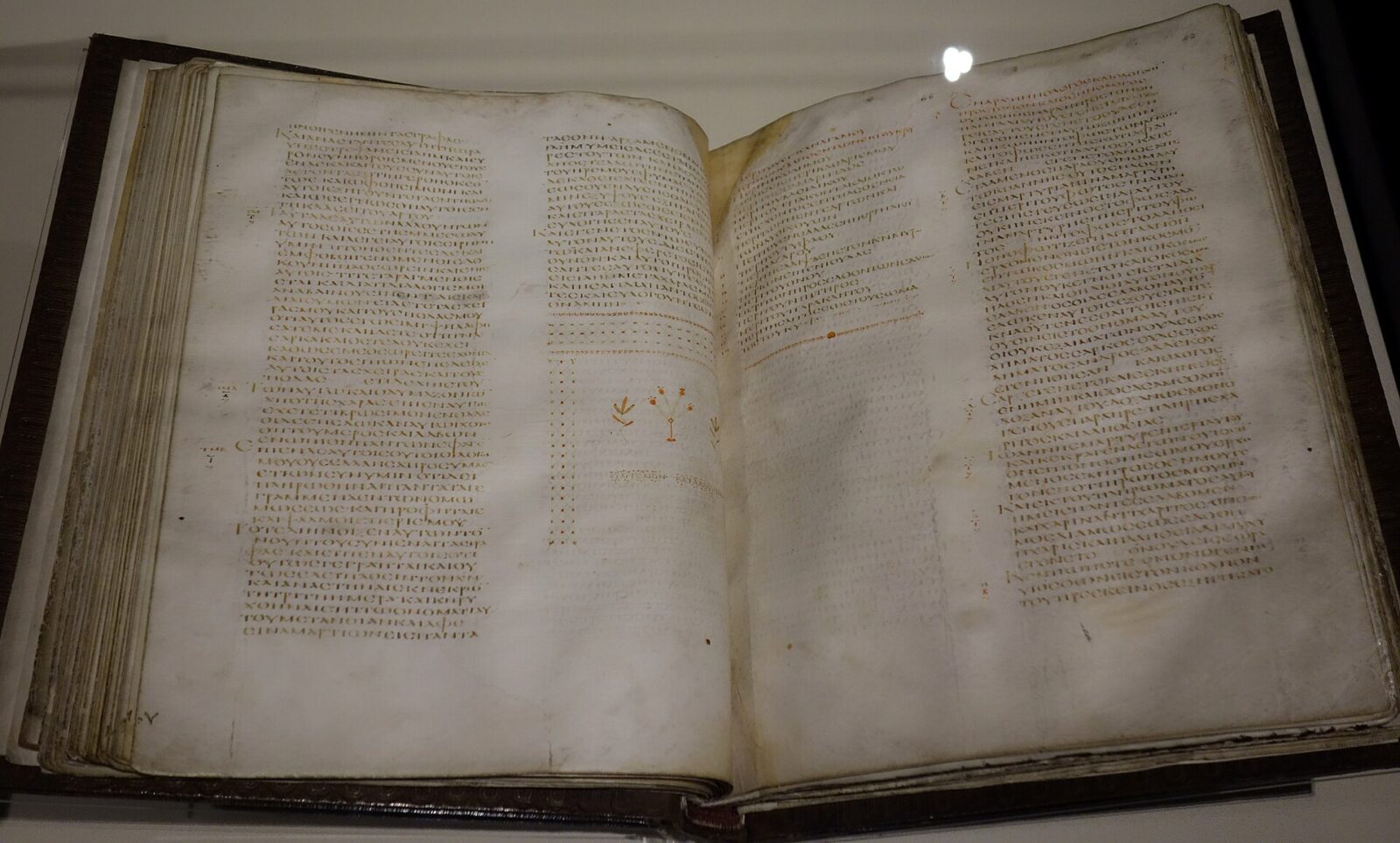 An open fifth-century Greek Bible manuscript in a museum case, showing columns of handwritten text.