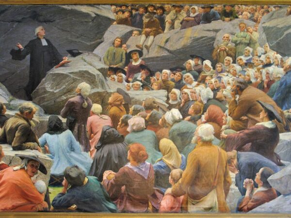 A Huguenot pastor preaches to a congregation gathered outdoors among rocks.
